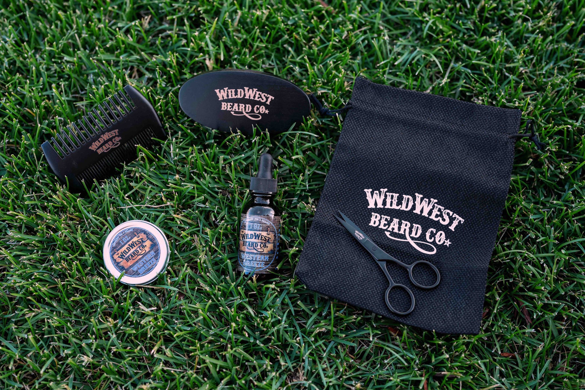 A clean picture of the Wild West Beard Co beard care starter kit contents on a nice healthy lawn background.  With a travel bag, beard comb, beard brush, natural beard oil, natural beard balm, and snipping scissors.